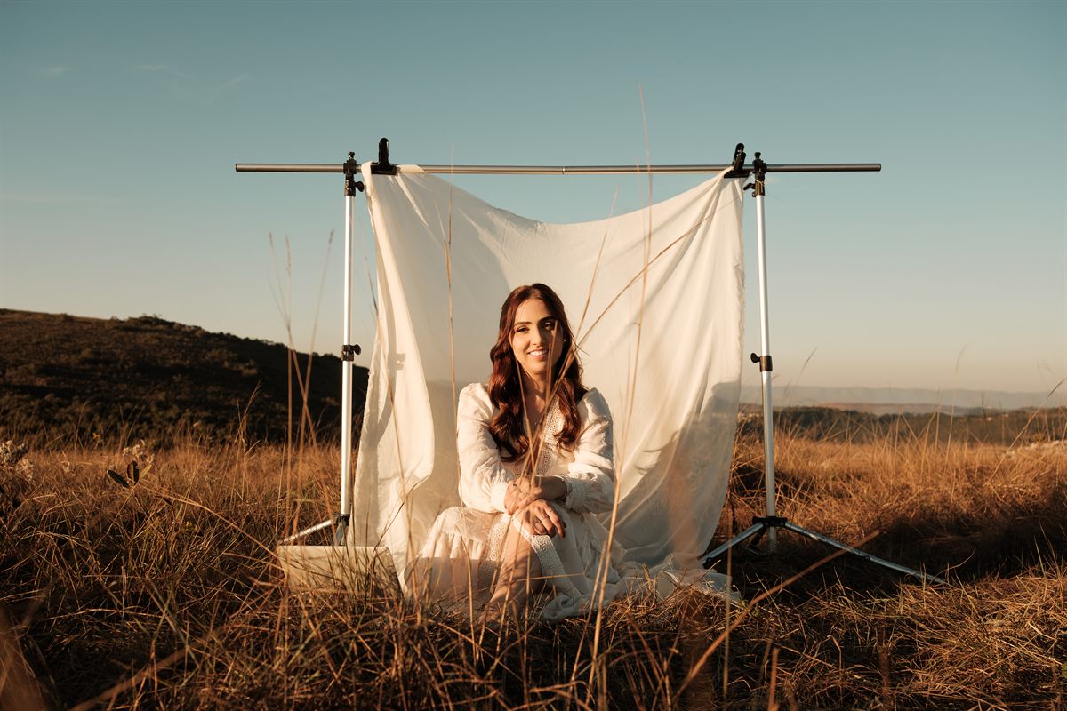 Luana Reis sentada em frente a um fundo branco de tecido, sorrindo